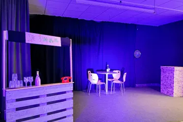 Die Theaterbühne mit einem Verkaufsstand, einem Tisch mit vier Stühlen und etwas zu Trinken.