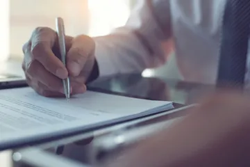 Person schreibt mit einem Stift auf Papier neben einem Laptop.