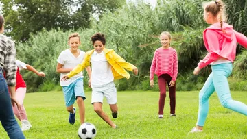 Mehrere Kinder rennen draußen und spielen Fußball.