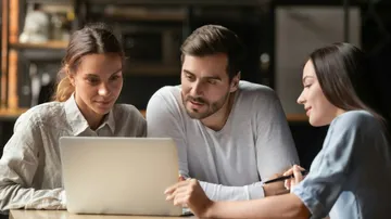 Drei Personen sehen zusammen etwas auf einem Laptop an.