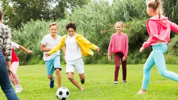 Mehrere Kinder rennen draußen und spielen Fußball.